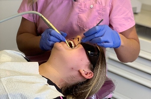 A female dental patient with blonde hair receiving treatment in a dental chair. The dentist has pink scrubs on.