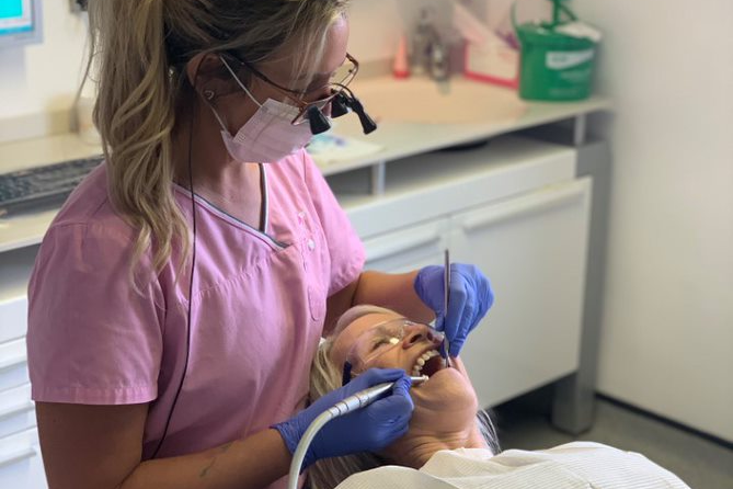 A dentist wearing dental loupes and a mask works on an elderly patient's teeth